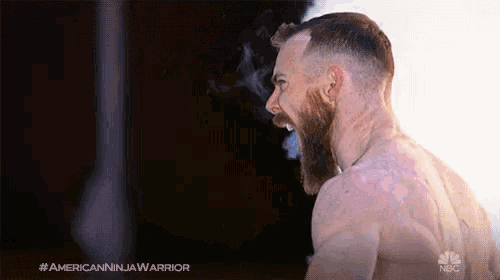 a shirtless man with a beard is smoking a cigarette and has the hashtag #americanninjawarrior