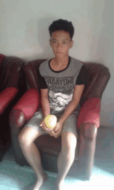 a young man wearing a parayon shirt sits on a couch