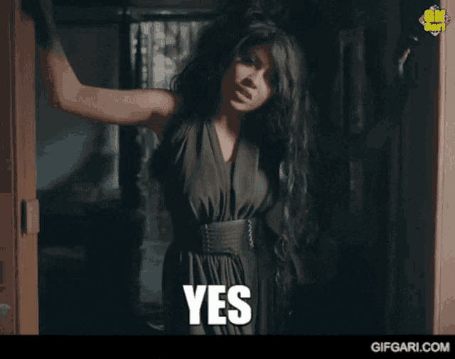a woman in a black dress is standing in front of a door and says yes