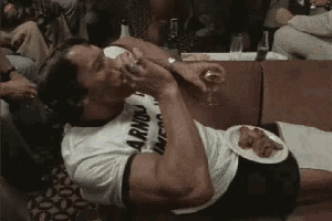 arnold schwarzenegger is laying on the floor eating food and drinking wine .