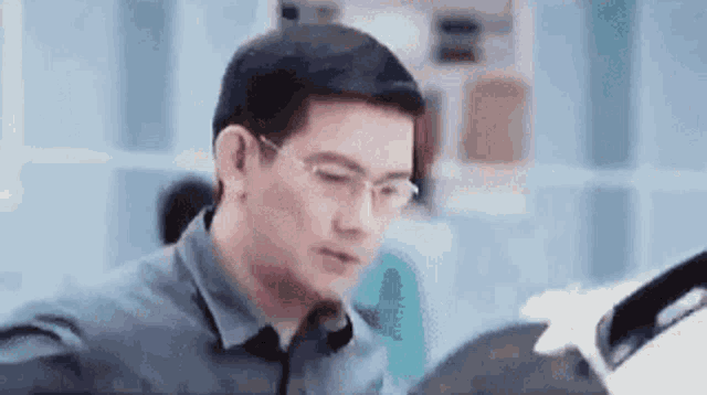 a man wearing glasses is sitting at a table in an office looking at something .