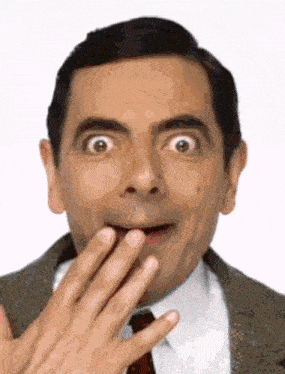 a man in a suit and tie is making a surprised face with his hand on his mouth .