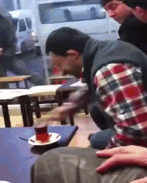 a man in a plaid shirt sits at a table with a cup of tea on it .