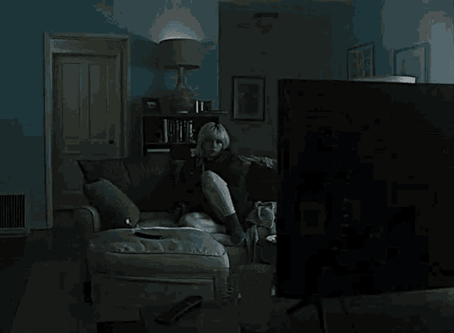 a woman is sitting on a couch watching tv in a dark room .