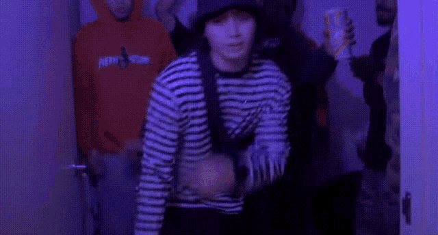 a group of young men are standing in a room with purple lights . one of the men is wearing a striped shirt .
