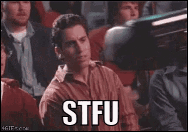 a man is sitting in a crowd of people with the words stfu written on his face .