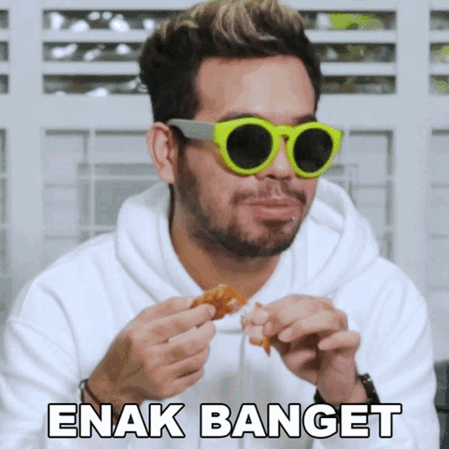 a man wearing green sunglasses is eating a piece of chicken with the words enak banget written on the bottom