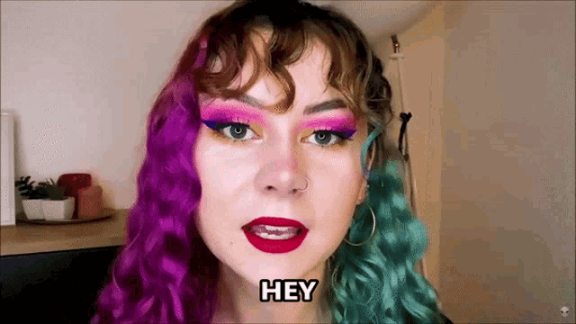 a woman with purple and green hair says " hey "