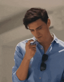 a man wearing a blue shirt and sunglasses lighting a cigarette