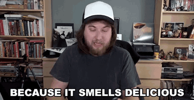 a man is sitting in front of a bookshelf and says because it smells delicious