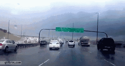 cars are driving down a highway in the rain with a green sign above them