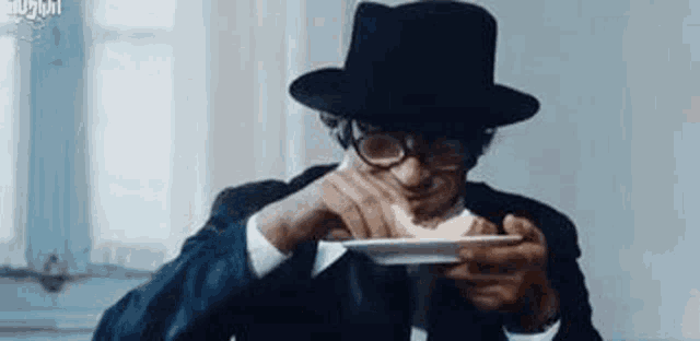 a man in a hat and glasses is holding a plate of food in his hand .