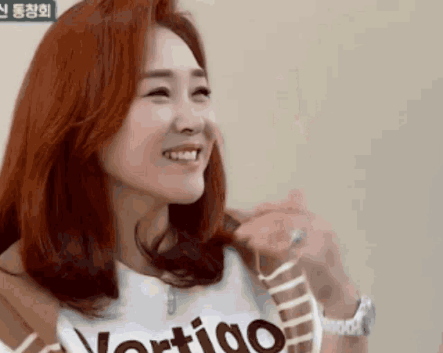 a woman with red hair is smiling and wearing a shirt that says vertigo