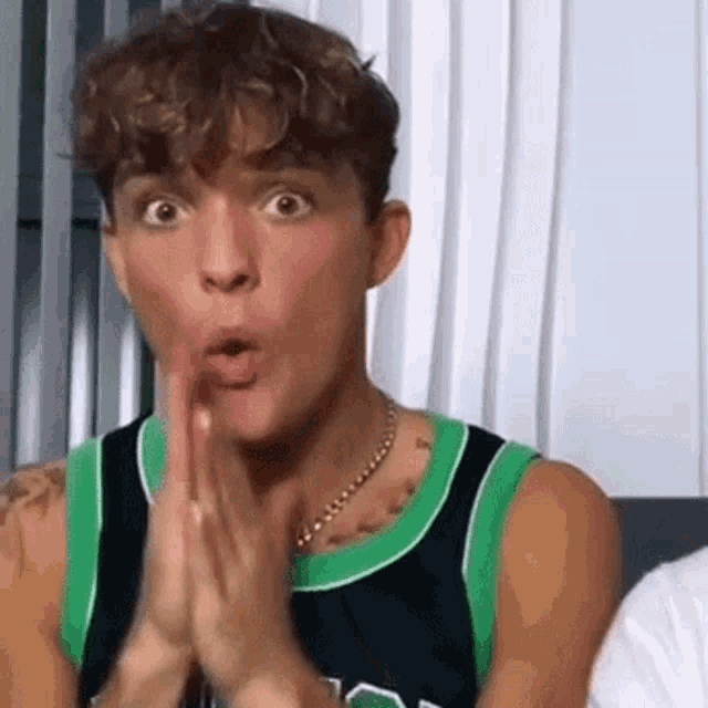 a young man is making a surprised face while sitting on a couch with his hands together .