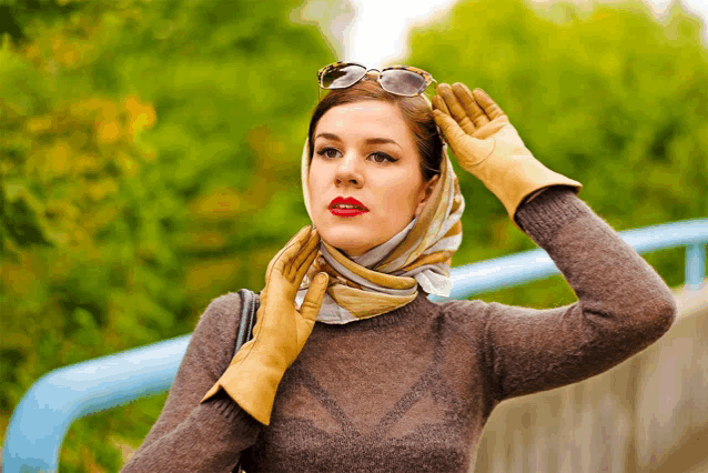 a woman wearing a scarf and gloves holds her hand to her face