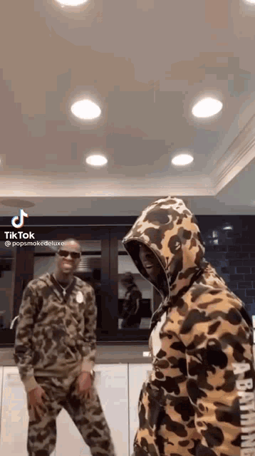a couple of men are standing next to each other in a kitchen wearing camouflage hoodies .