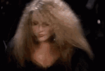 a woman with very long blonde hair is standing in a dark room with her hair blowing in the wind .
