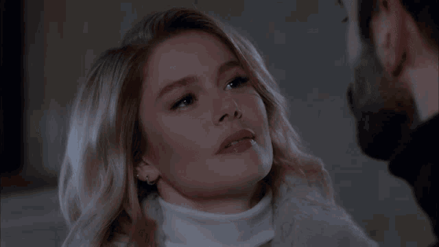 a woman in a white turtleneck looks at a man