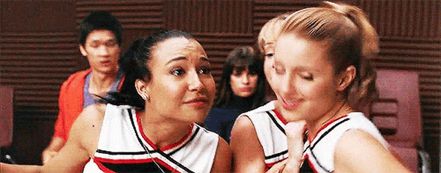 two cheerleaders are standing next to each other in a room with a group of people .