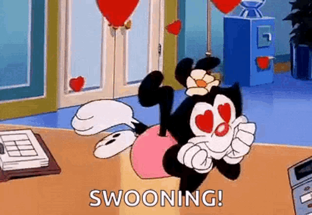 a cartoon character with heart shaped eyes is laying on a table with balloons in the background .