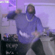 a man in a blue hoodie is dancing in a room with purple walls