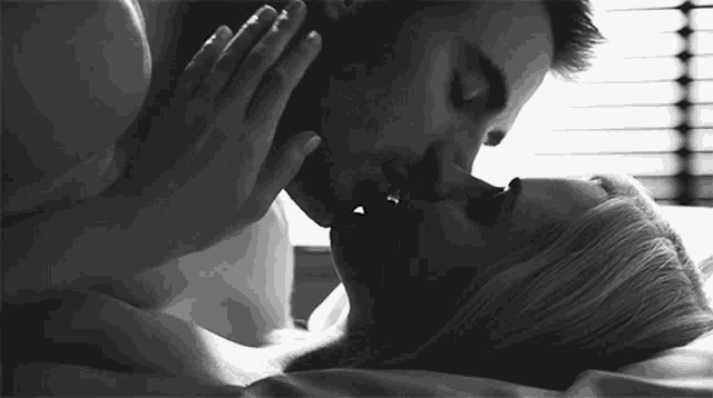 a black and white photo of a man and woman kissing in bed