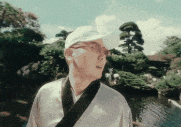 a man wearing a white hat and sunglasses is standing in front of a pond