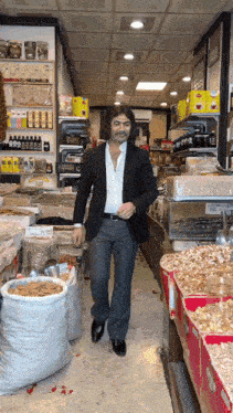 a man in a suit walks down a store aisle filled with bags of food