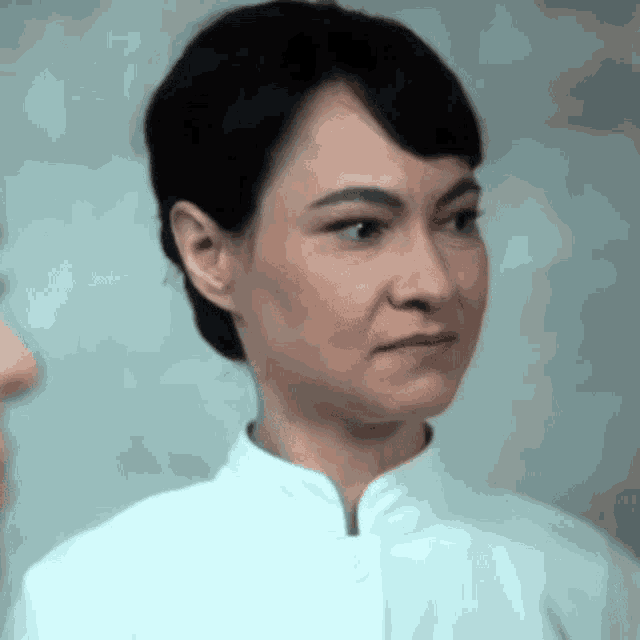 a woman with short hair is wearing a white coat and making a funny face .
