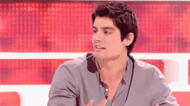 a man wearing a grey shirt is sitting in front of a red background .