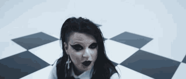 a woman in a white shirt and black vest is sitting on a black and white checkered floor .