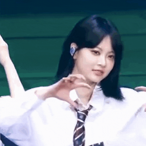 a girl in a white shirt and tie is making a heart with her hands .