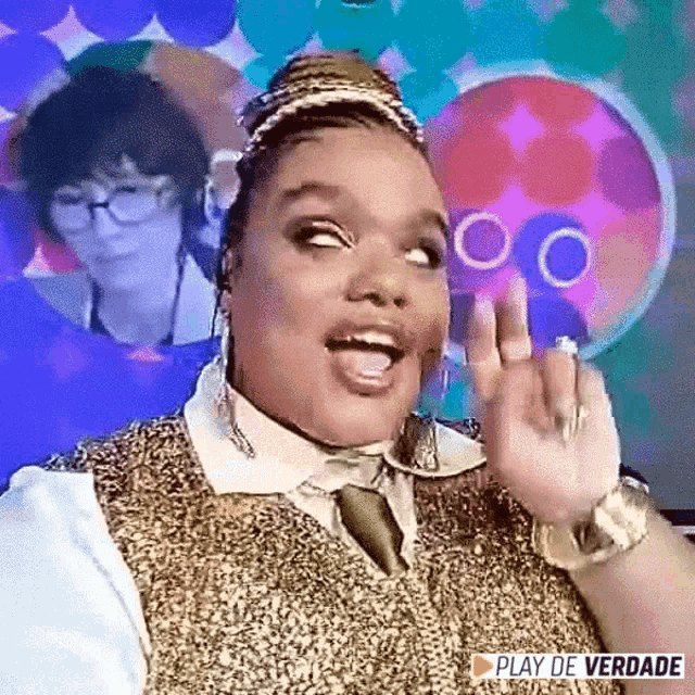 a woman in a gold vest and tie is making a funny face and waving .