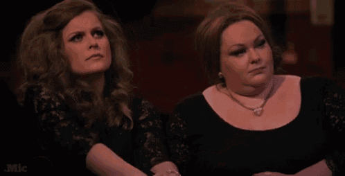 two women are sitting next to each other in a dark room looking at something .