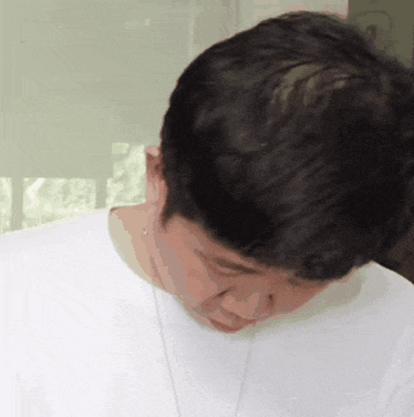 a man wearing a white shirt and a necklace looks down