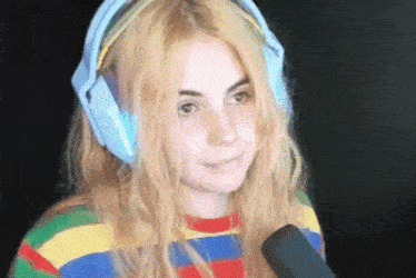 a woman wearing headphones and a striped shirt is smiling and holding a microphone .