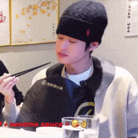 a man wearing a black hat is holding chopsticks in front of a sign that says sesame rouge