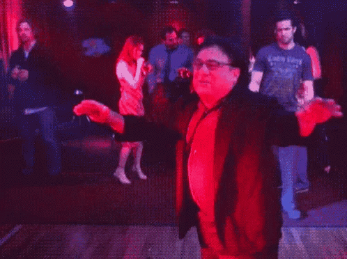 a man in a red jacket and tie is dancing in a dark room