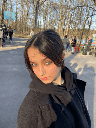 a girl wearing a black hoodie stands in front of a basketball hoop