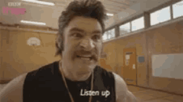 a man with a mustache wearing a black shirt that says listen up