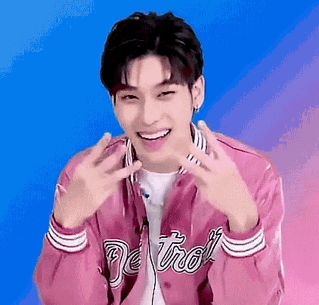 a young man is wearing a pink jacket and making a peace sign .