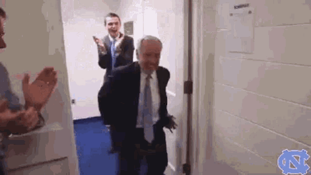 a man in a suit and tie is walking through a doorway while two other men applaud .