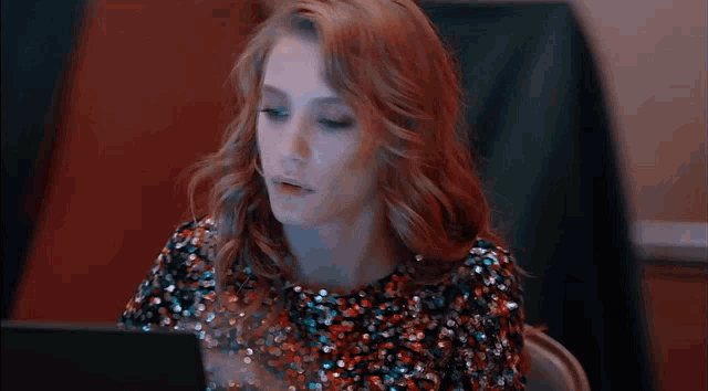 a woman in a sequined dress is covering her face with her hand while sitting in front of a laptop computer .