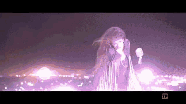 a woman in a purple dress is standing in front of a microphone in a dark room .