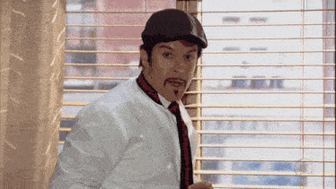 a man wearing a hat and tie is looking out a window