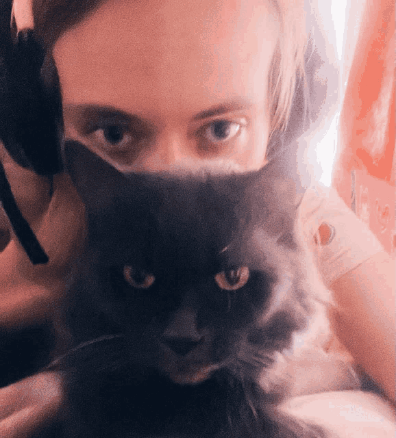 a woman wearing headphones holds a cat in front of her face