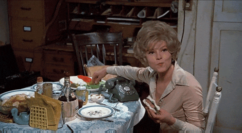 a woman sits at a table with a phone and a sandwich in her hand