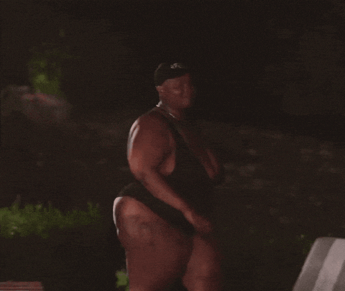 a woman in a black bathing suit is standing in the dark .