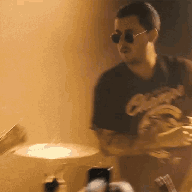 a man wearing sunglasses and a black shirt is playing drums in a room .