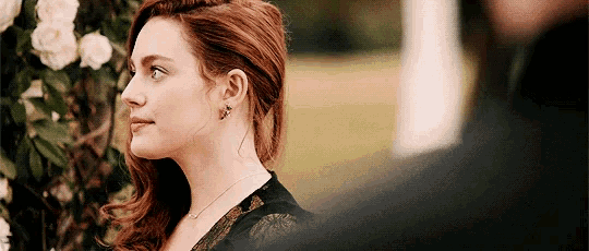 a woman with red hair is wearing earrings and a necklace and looking at a man .